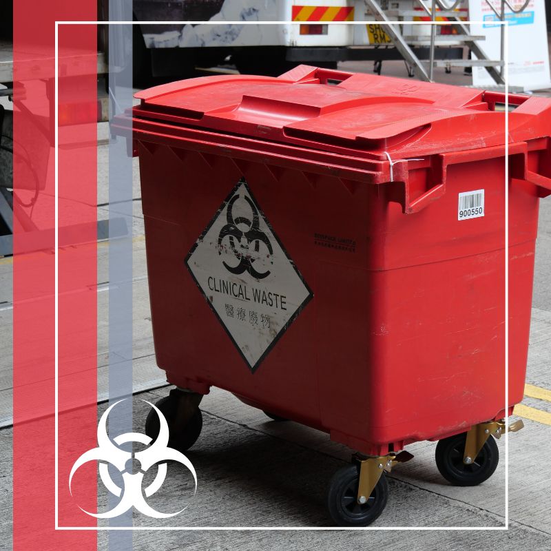 A large red medical waste bin with wheels, marked with a biohazard symbol, sitting outdoors.